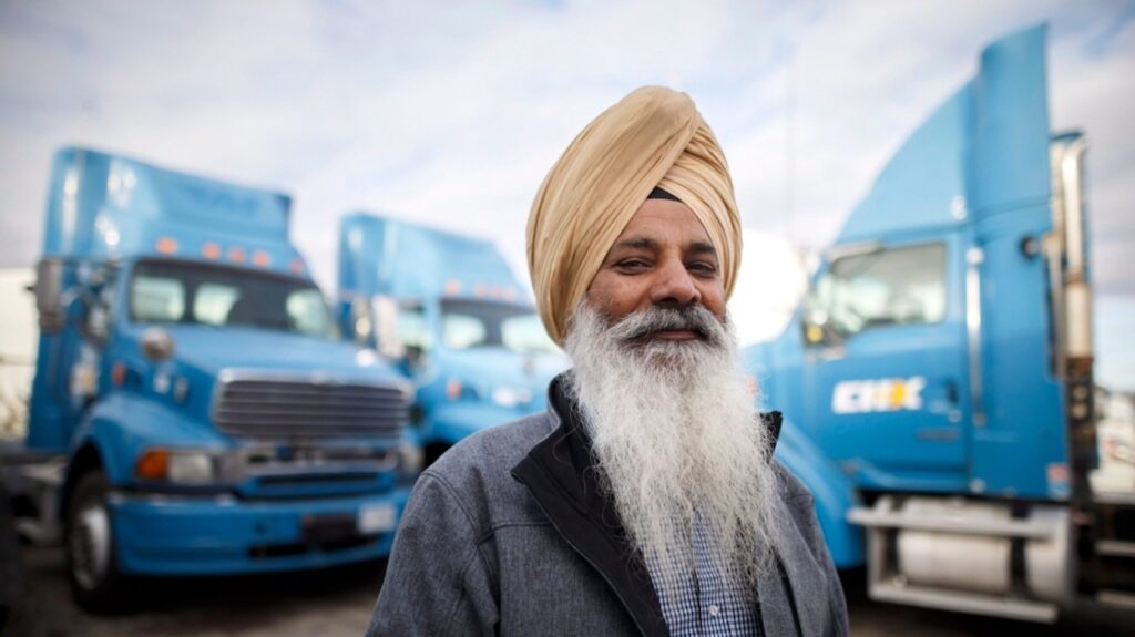 Indian-sikh-truck-driver-standing-in-front-of-blue-trucks-in-america